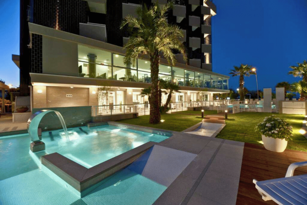 Ein beleuchteter Swimming Pool vor einer Palme und einem Hotelgebäude
