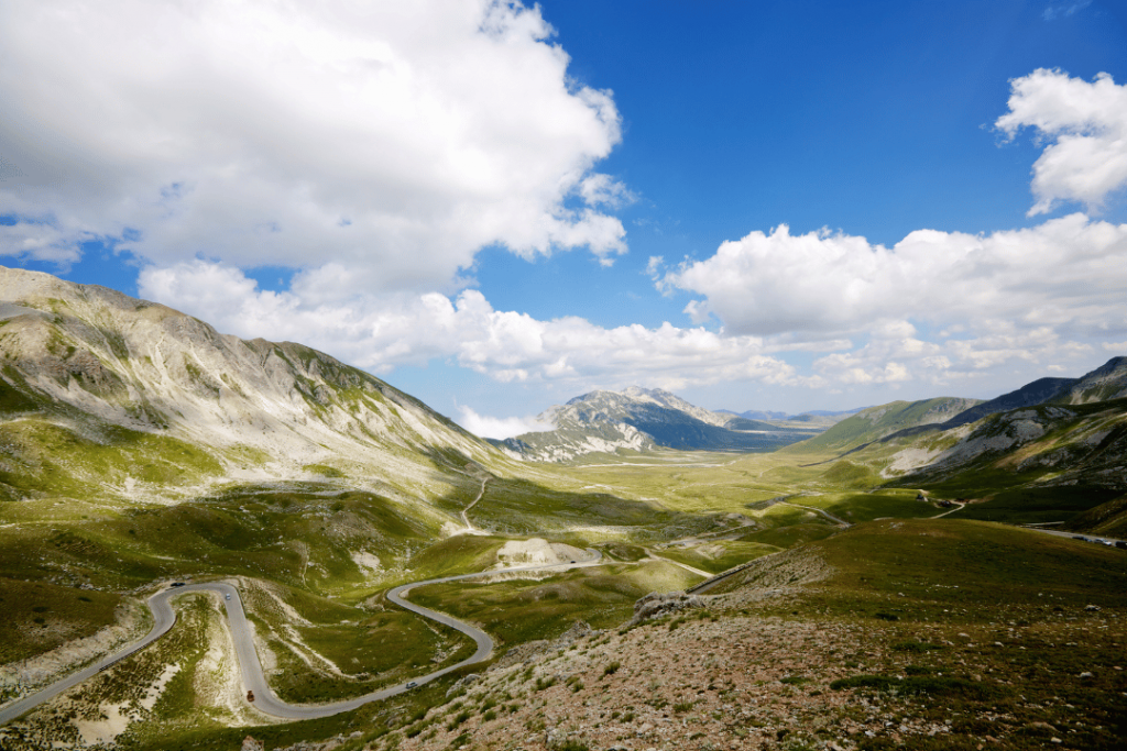 Eine Straße schlängelt sich durch grüne Wiesen und Berge am Campo Imperatore