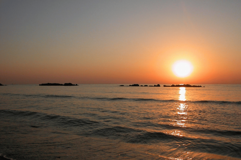 Eine orange-gelber Sonne über dem Meer