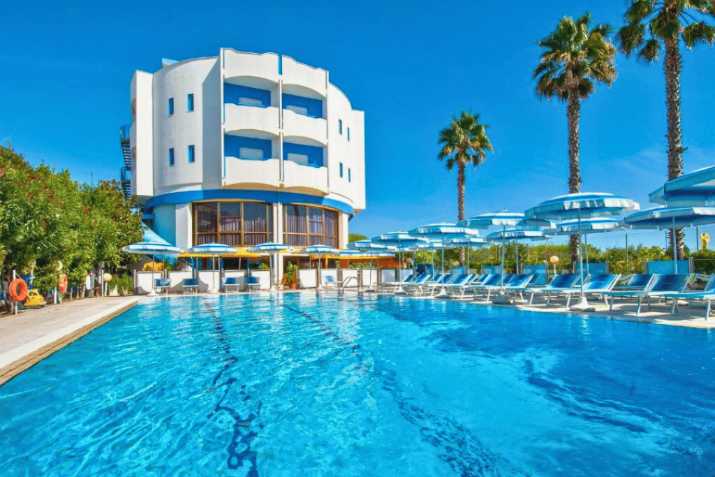 Ein Hotel mit Swimming Pool, Liegen, Sonnenschirmen und Palmen in Martinsicuro