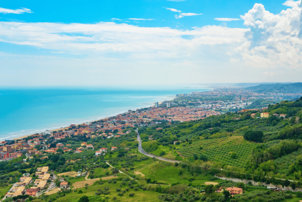 Bewaldete Hügel, rote Dächer einer Stadt und hellblaues Meer