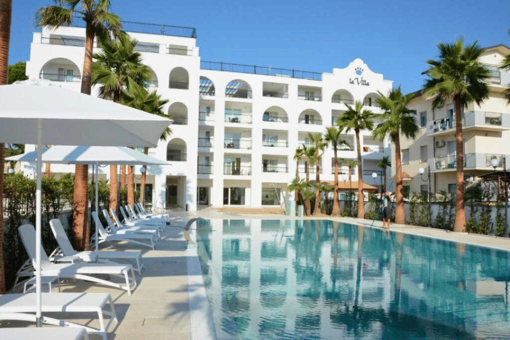 Ein Swimmingpool mit Liegen und Palmen vor einem Apartmentkomplex